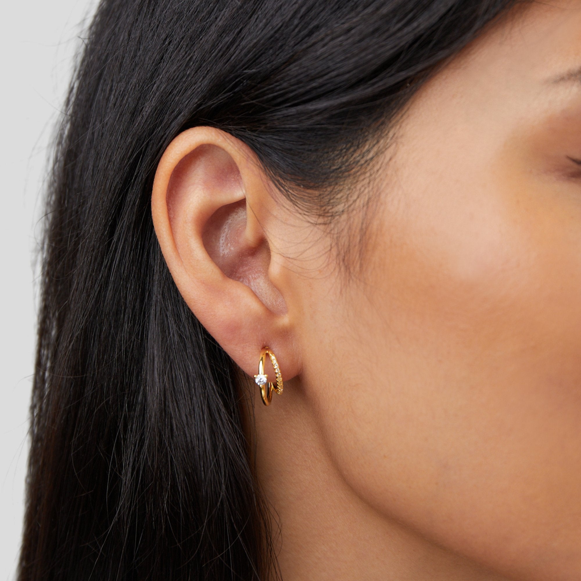 Layered Crystal Gold Hoop Earrings, worn on an ear, two gold hoops with a small clear stone