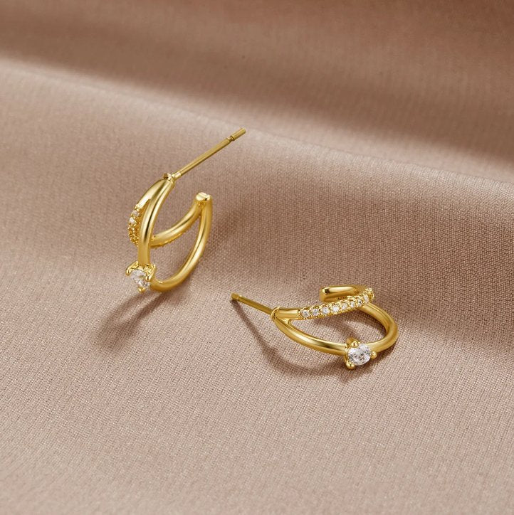 Layered Crystal Gold Hoop Earrings, a pair of gold hoops lying on a beige satin cloth, one