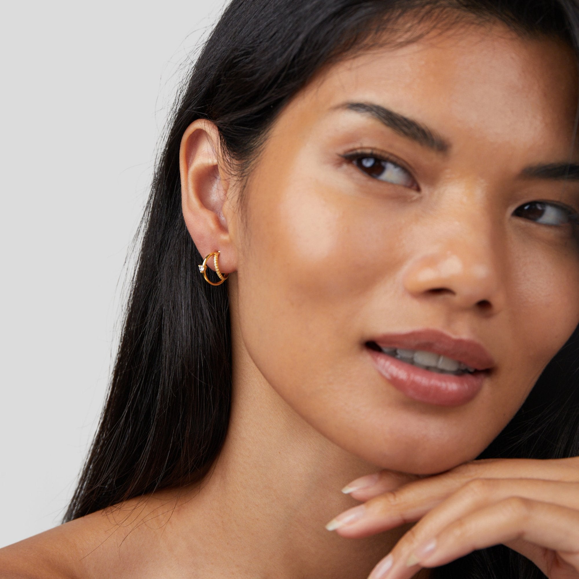 Layered Crystal Gold Hoop Earrings, worn on an ear by a model with long dark hair, hand near chin