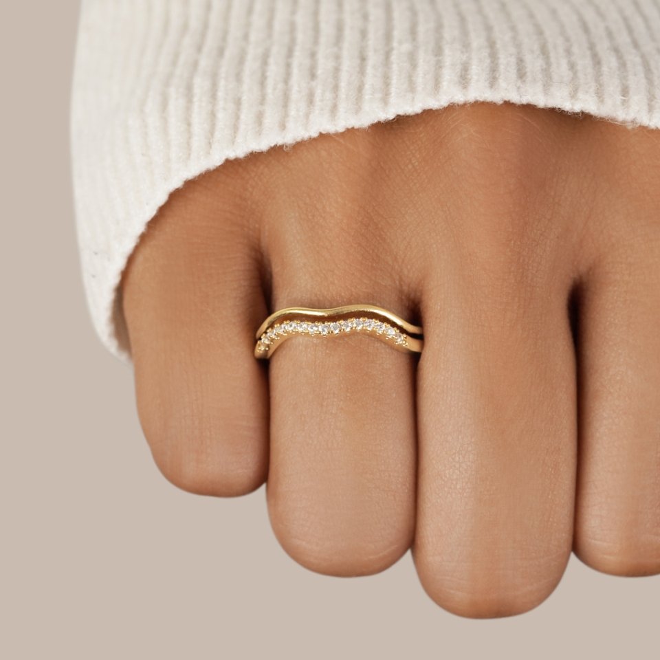 Layered Juni Gold & Crystal Ring, worn on a finger with a cream knit sleeve, wavy band