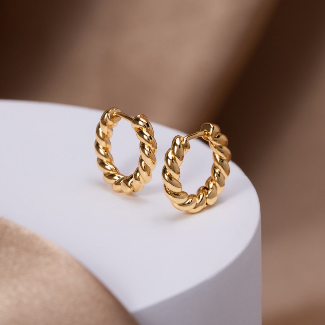 Layla Gold Twist Earrings, a pair of twisted gold hoops resting on a white pedestal