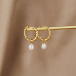 Layla Pearl Twist Earrings, pair of twisted gold hoops with pearl drops, resting on a gold bar