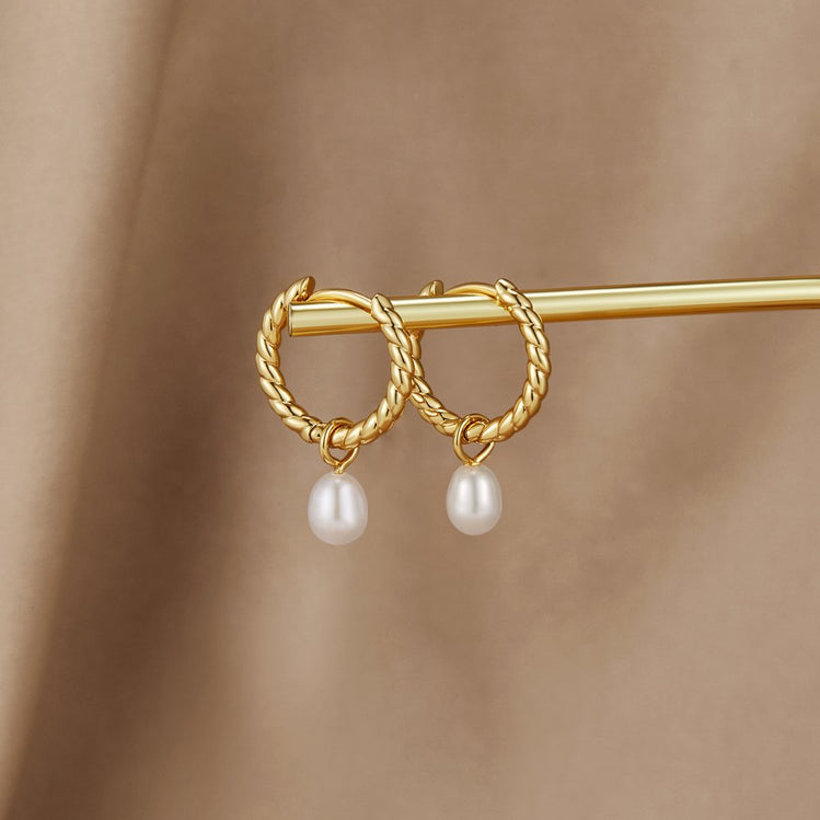 Layla Pearl Twist Earrings, pair of twisted gold hoops with pearl drops, resting on a gold bar