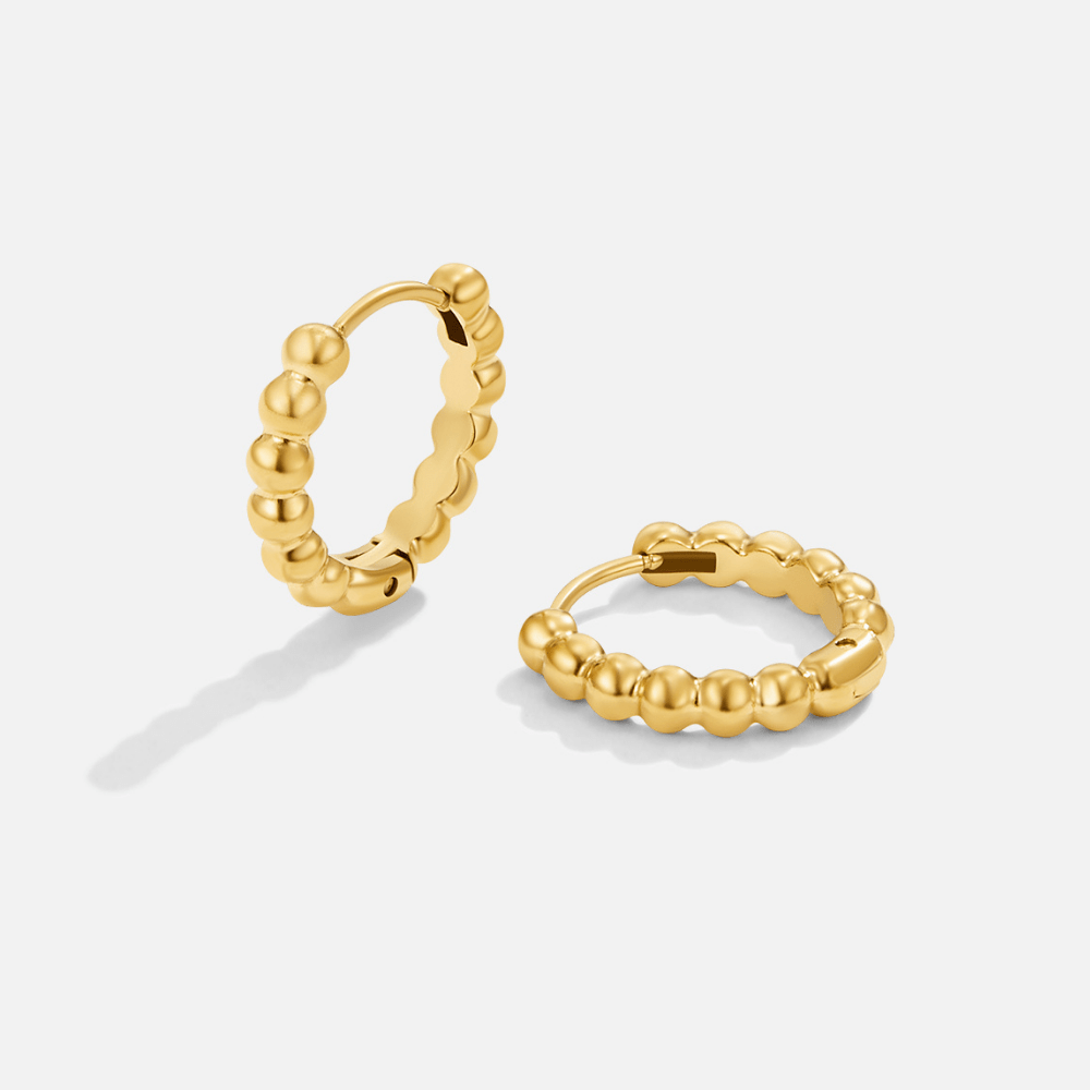 Leona Gold Bead Hoop Earrings, pair of gold beaded hoops standing on a white surface, one tilted