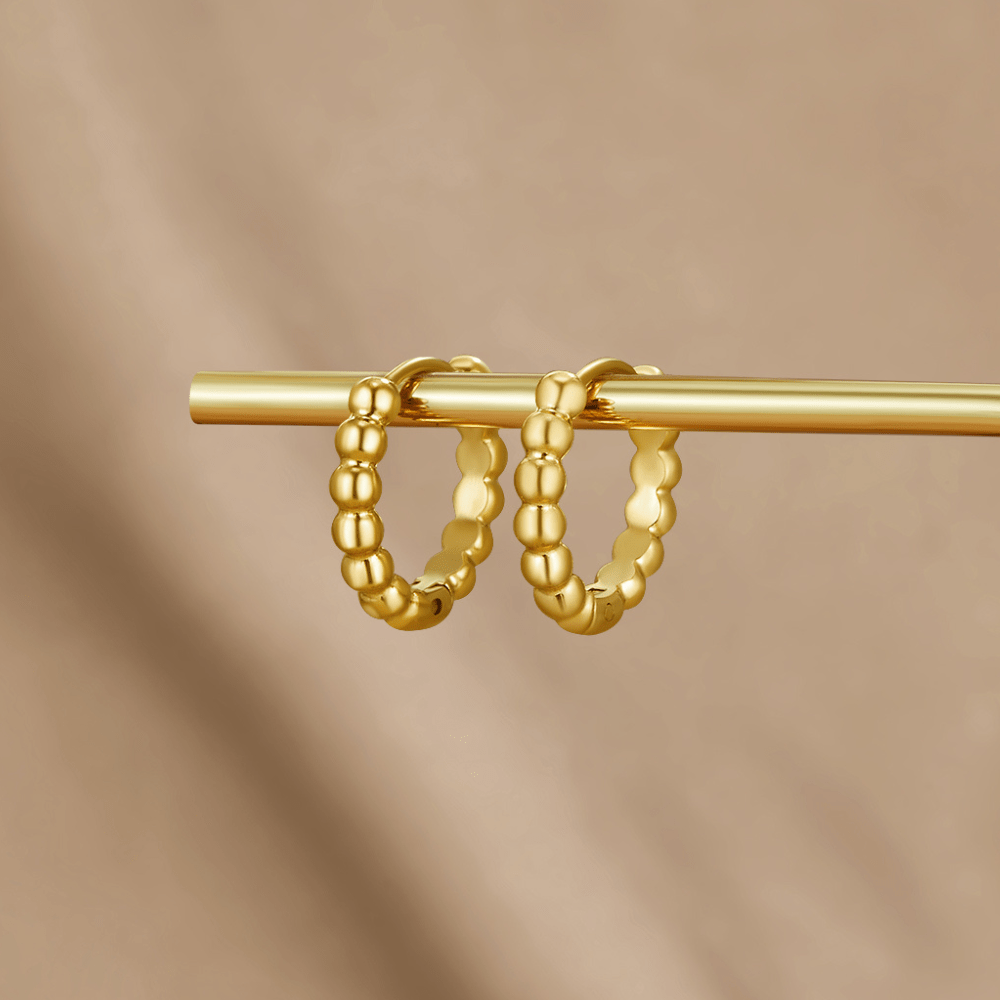 Leona Gold Bead Hoop Earrings, a pair of gold beaded hoops hanging on a gold bar against beige