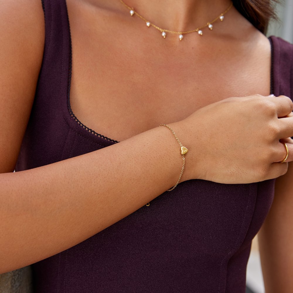 Letter Heart Bracelet, worn on a wrist with a gold heart charm and pearl necklace