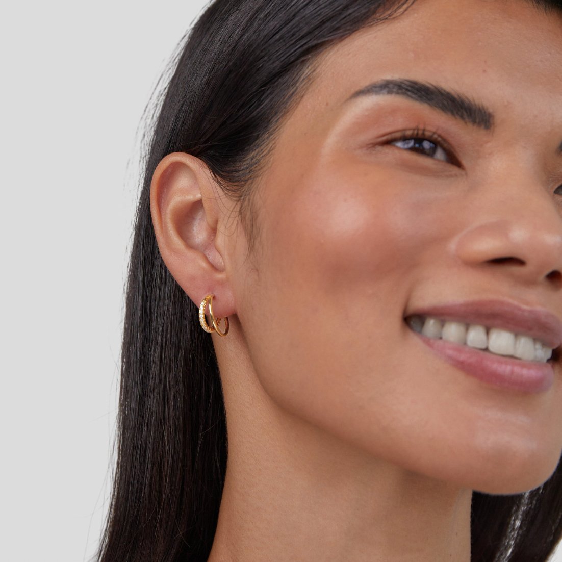 Leyla Crystal Double Hoop Earrings, worn on an ear by a smiling woman with long dark hair