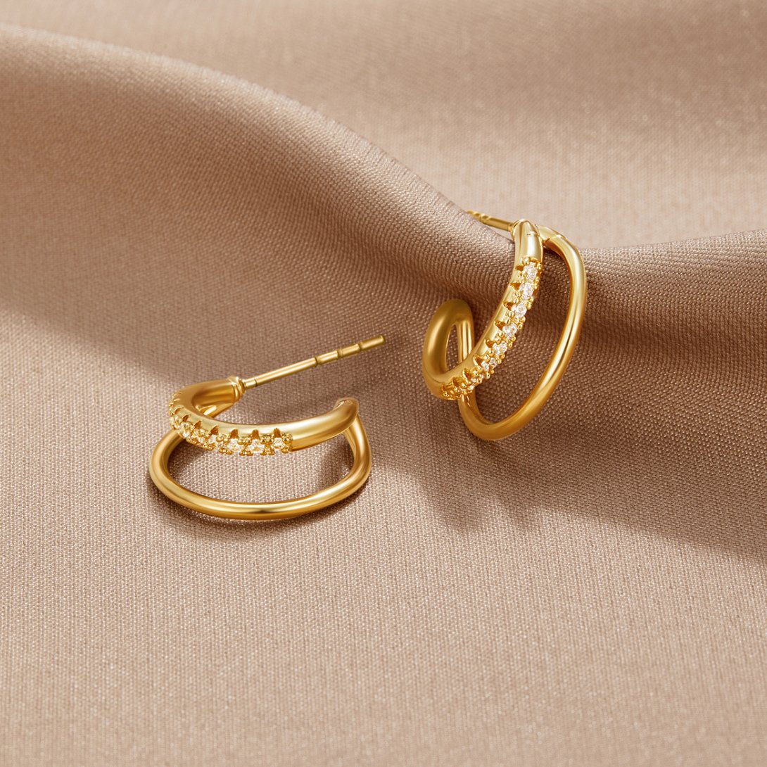 Leyla Crystal Double Hoop Earrings, pair of gold double hoop earrings on a beige satin cloth, one lying flat and one angled