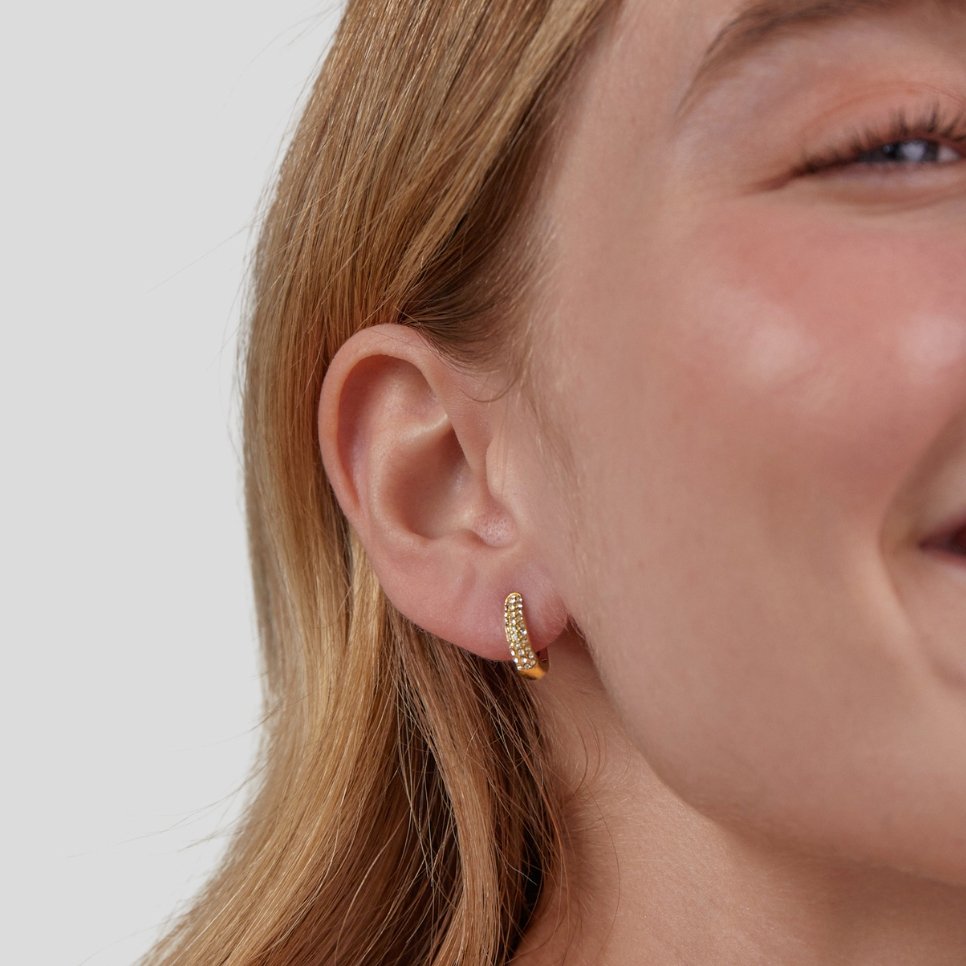 Lily Crystal Hoop Earrings, worn on an ear of a smiling woman with long hair