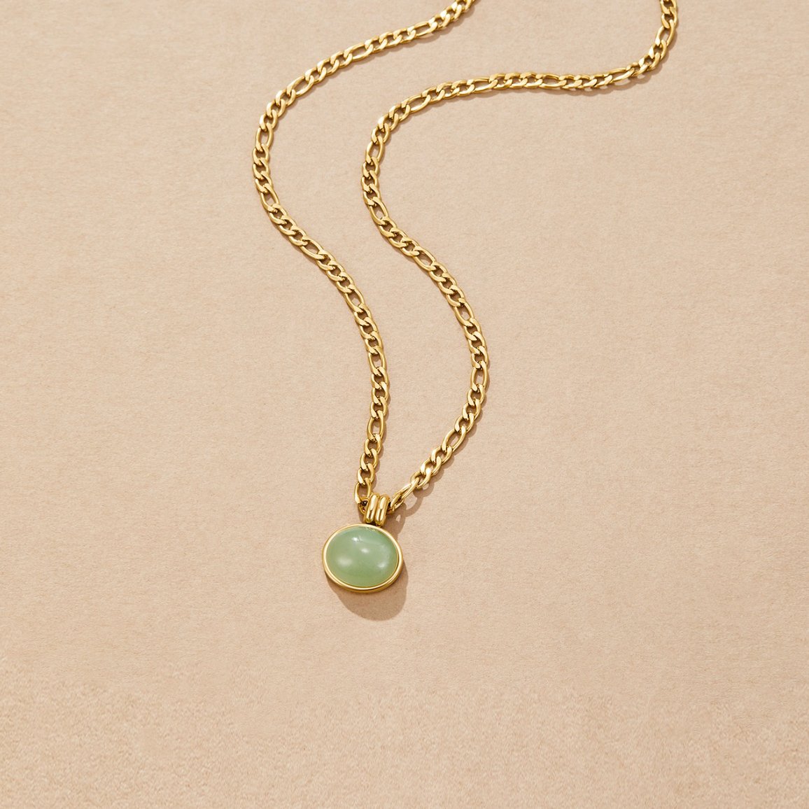 Liza Jade Pendant Necklace, laid flat on beige suede, gold chain with green oval pendant