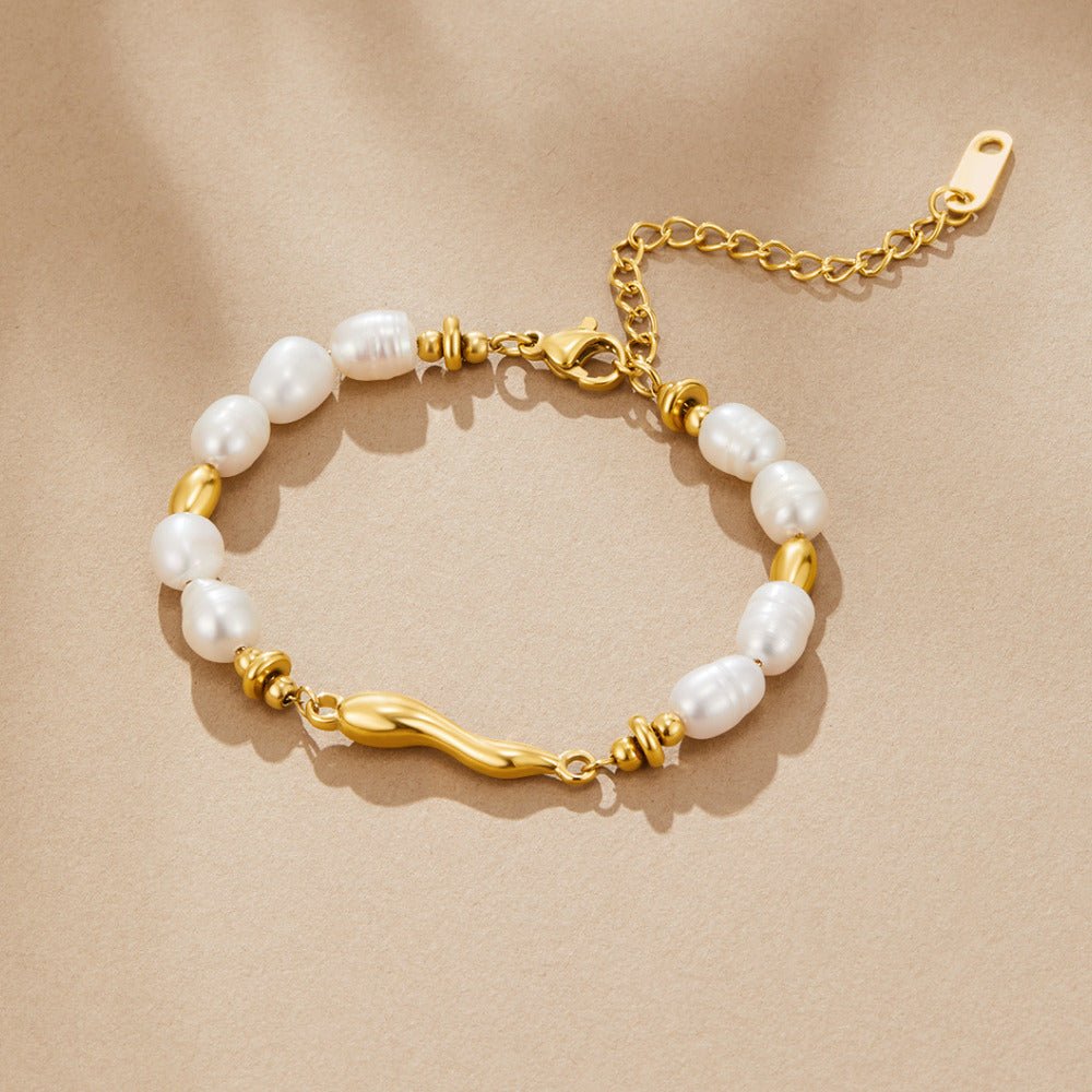 Lovina Pearl Bracelet, laid flat on beige fabric, white pearls and gold beads, wavy gold bar