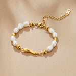 Lovina Pearl Bracelet, laid flat on beige fabric, white pearls and gold beads, wavy gold bar