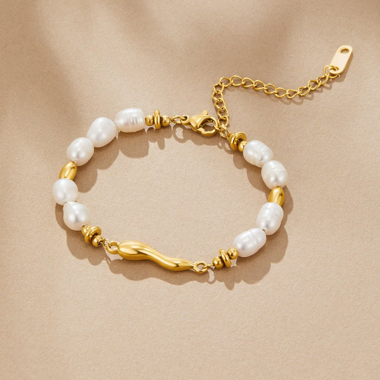 Lovina Pearl Bracelet, laid flat on beige fabric, white pearls and gold beads, wavy gold bar