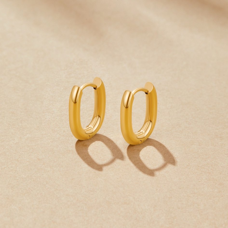 Madison Gold Hoop Earrings, a pair of oval gold hoops on a beige surface, side view