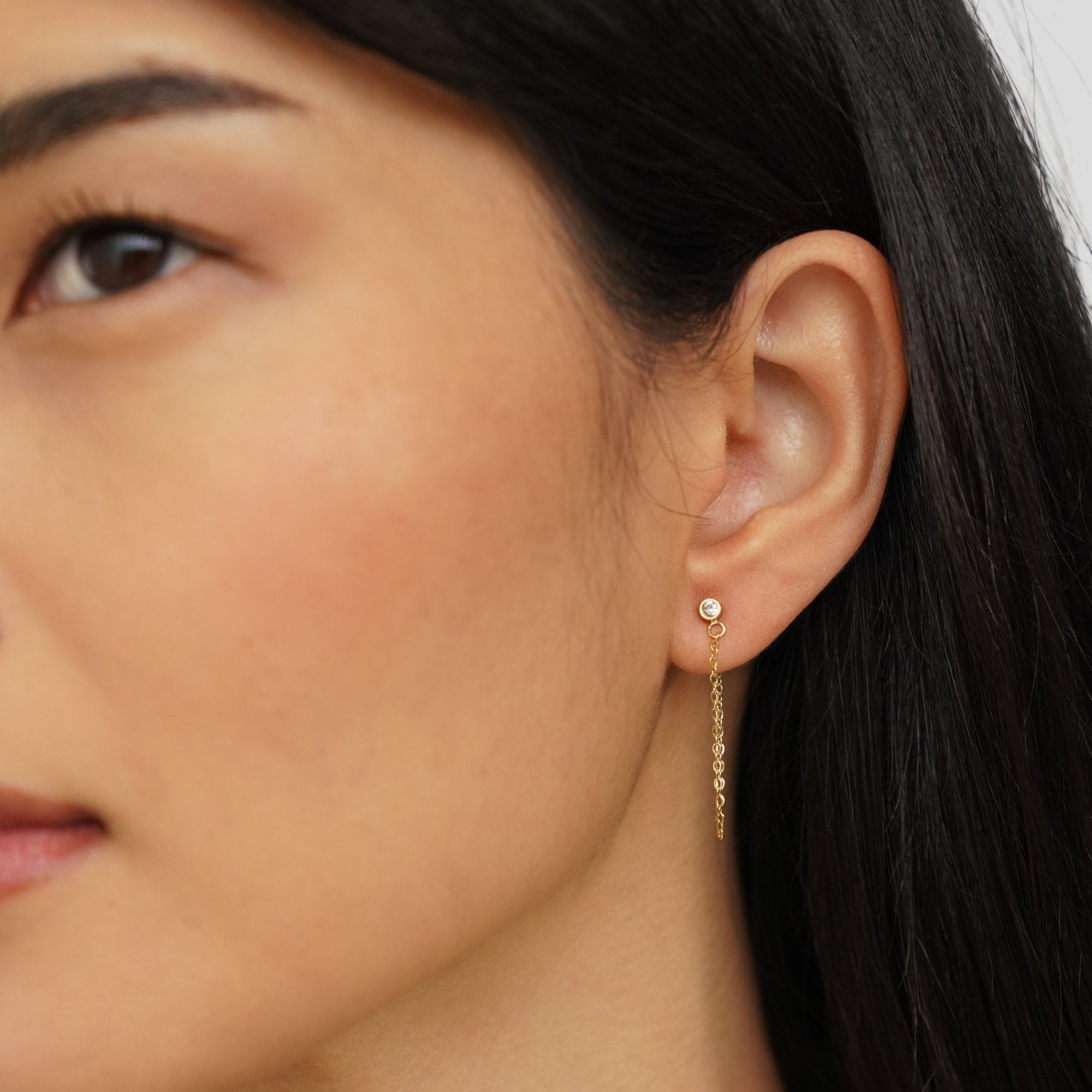 Mara Crystal Chain Earrings, worn on an ear, with a small round stone stud and gold chain drop