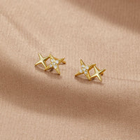 Midnight Magic Studs, pair of gold star studs on a beige fabric, one with small clear stones