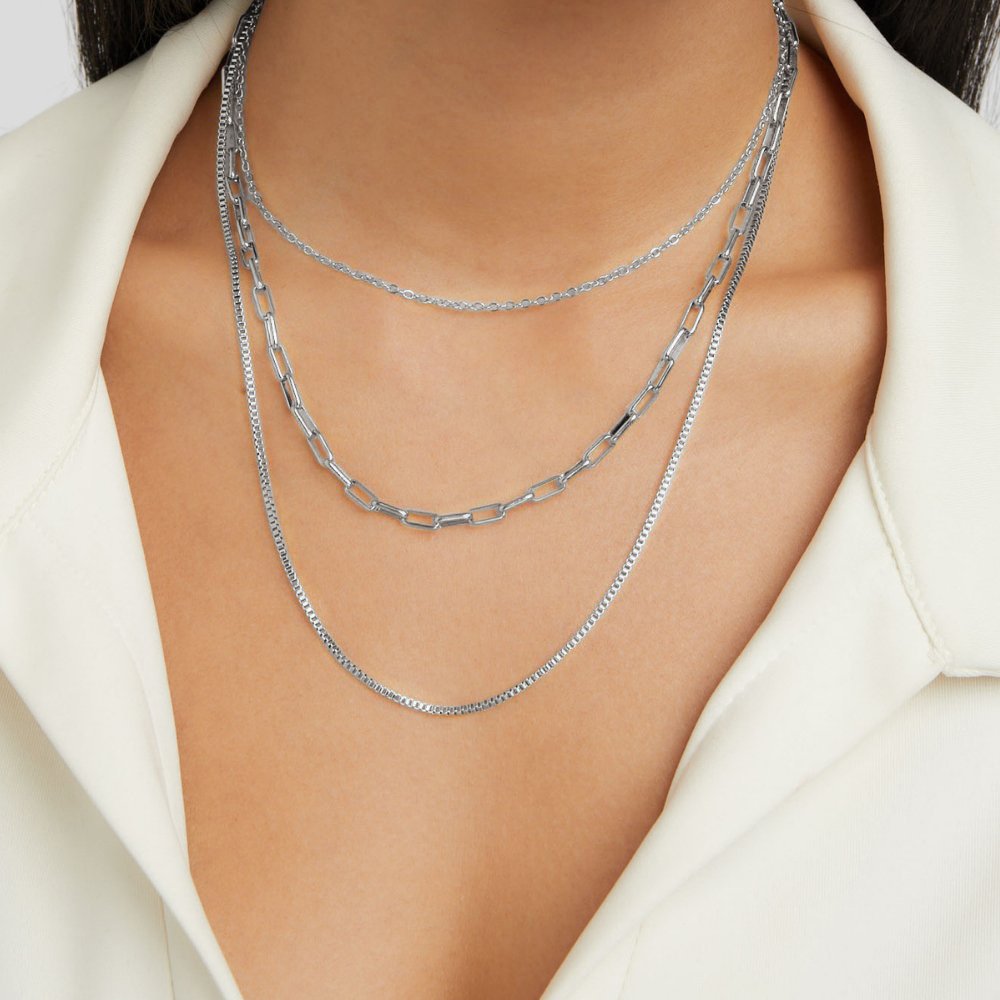 Miela Layered Chain Necklace, worn on a neck with three layered silver chains over a white collar