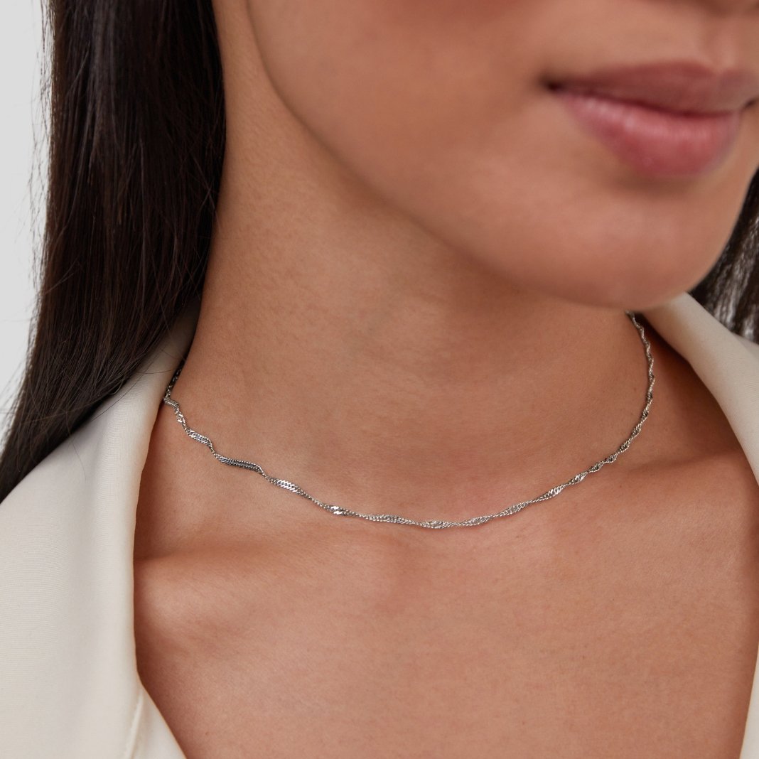 Mila Twist Silver Chain Necklace, worn on a woman's neck with a cream jacket, close crop
