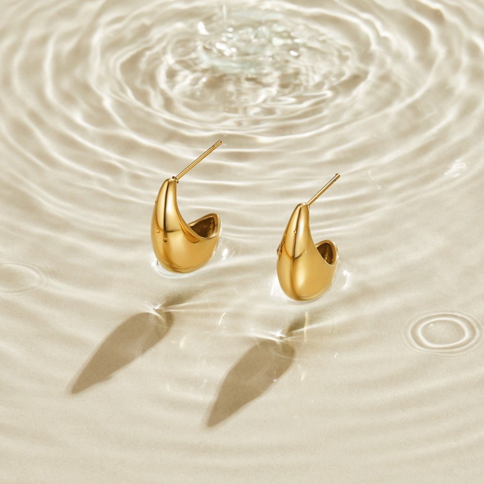 Mini Curved Gold Hoops, a pair of gold earrings resting on rippled water, casting shadows