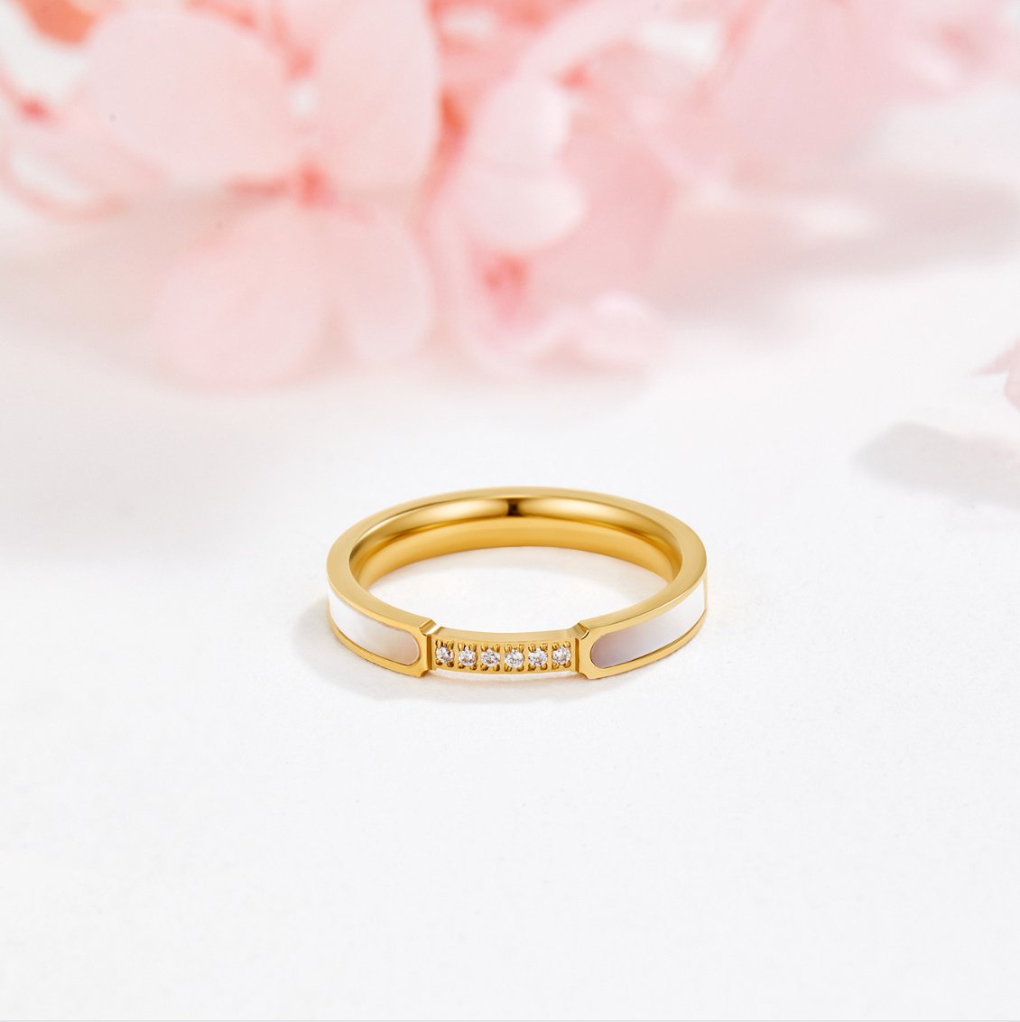 Mother Of Pearl & Crystal Ring, gold band standing upright on white surface, pink flowers behind