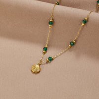 Nerissa Gold Shell & Green Bead Necklace, laid on beige fabric, gold shell pendant with green