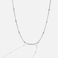 Niyah Bead Silver Chain Necklace, laid out on a light grey surface, silver chain with evenly