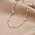 Nura Pearl 18K Gold Necklace, laid flat on draped beige satin, gold chain with white pearls