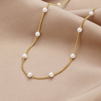 Nura Pearl 18K Gold Necklace, laid flat on draped beige satin, gold chain with white pearls
