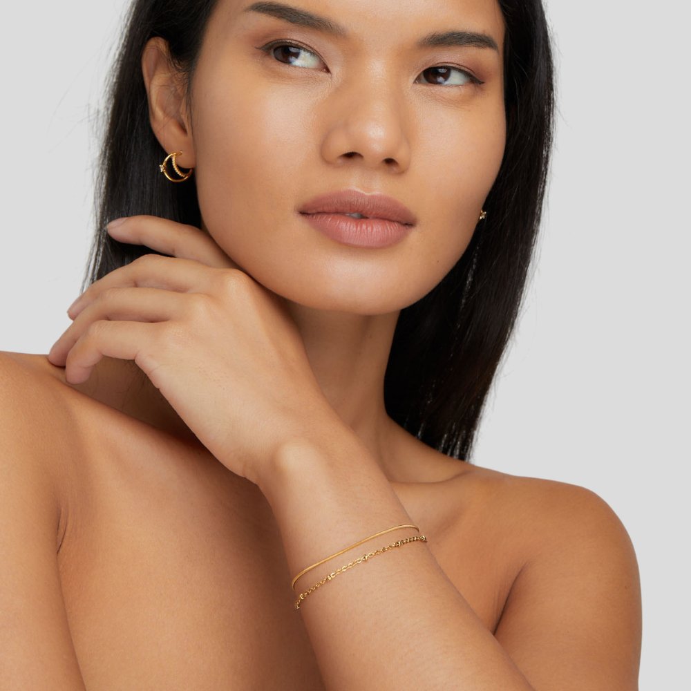 Pia Gold Layered Bracelet, worn on a wrist with a gold hoop earring, hand near neck