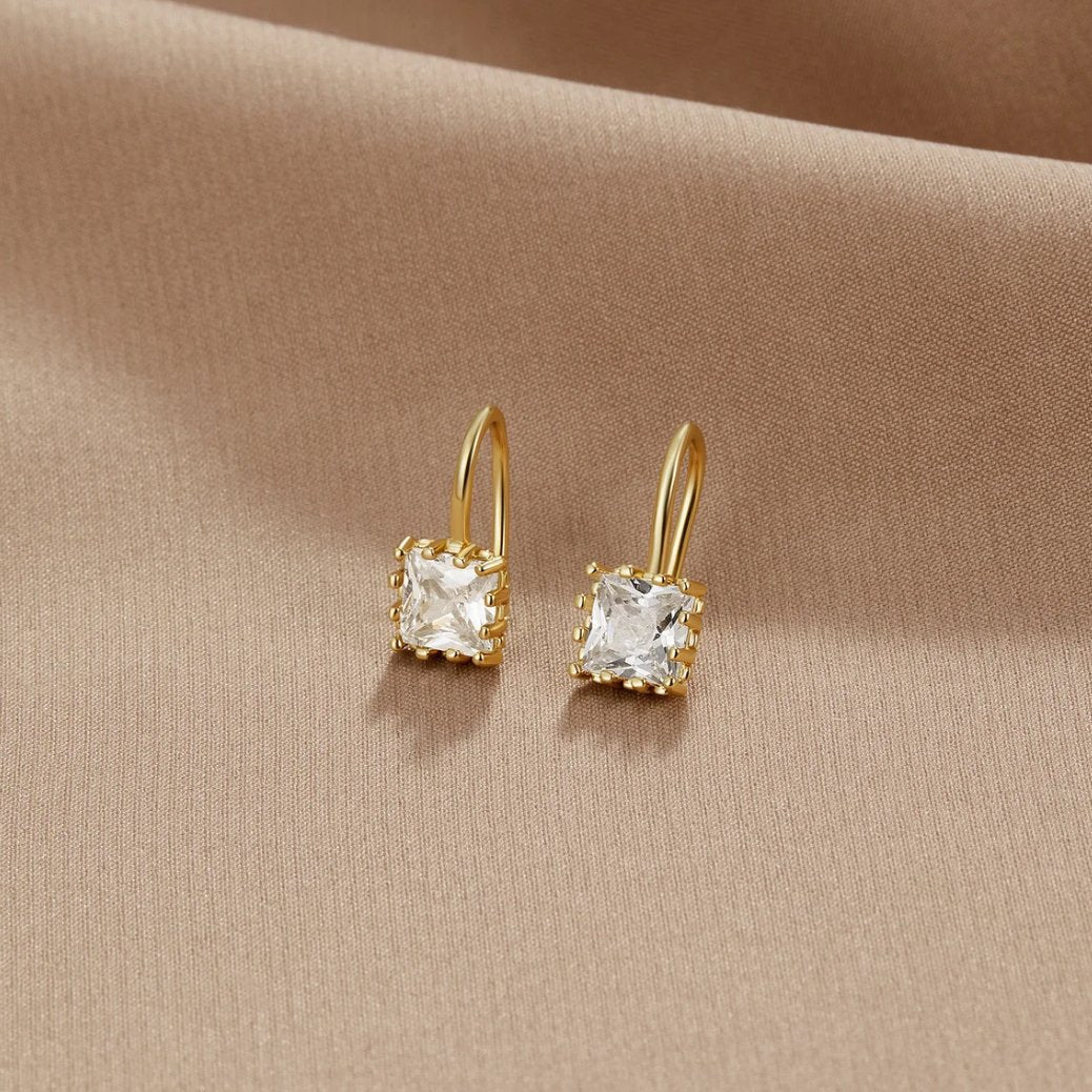 Piper Crystal Drop Earrings, pair of gold earrings with square clear stones on beige fabric