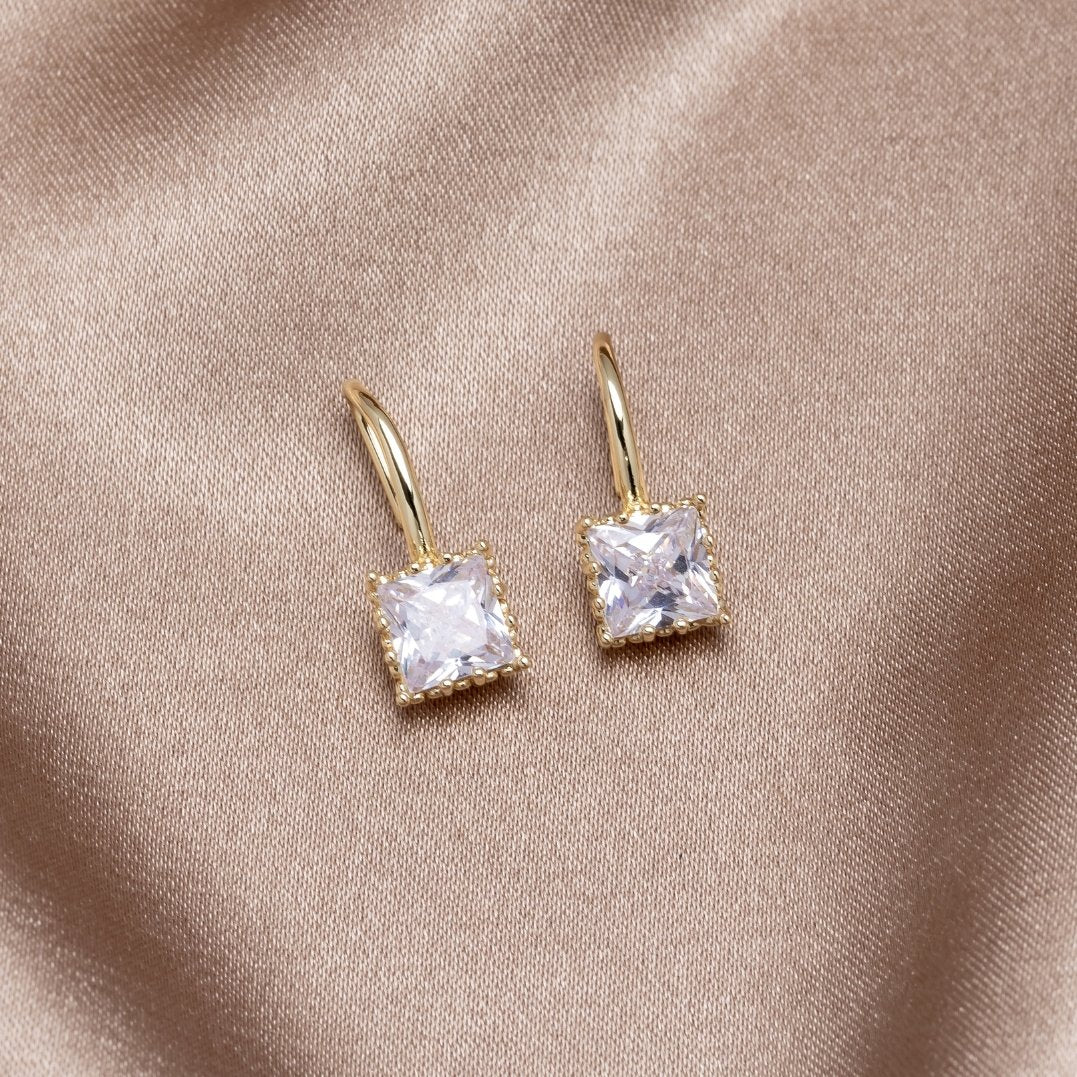 Piper Crystal Drop Earrings, pair of gold earrings with square clear stones on beige satin