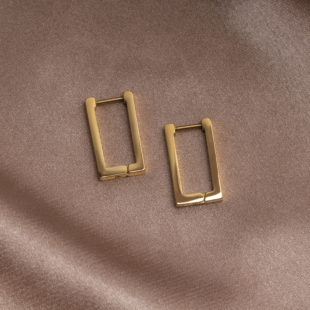 Gold Rectangle Hoop Earrings, pair of rectangular gold hoops lying on a taupe satin cloth
