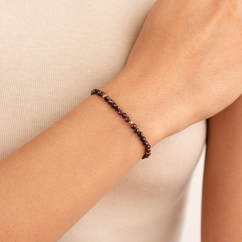 Red Garnet Bead Bracelet, worn on a wrist against a cream ribbed top, with gold accent beads