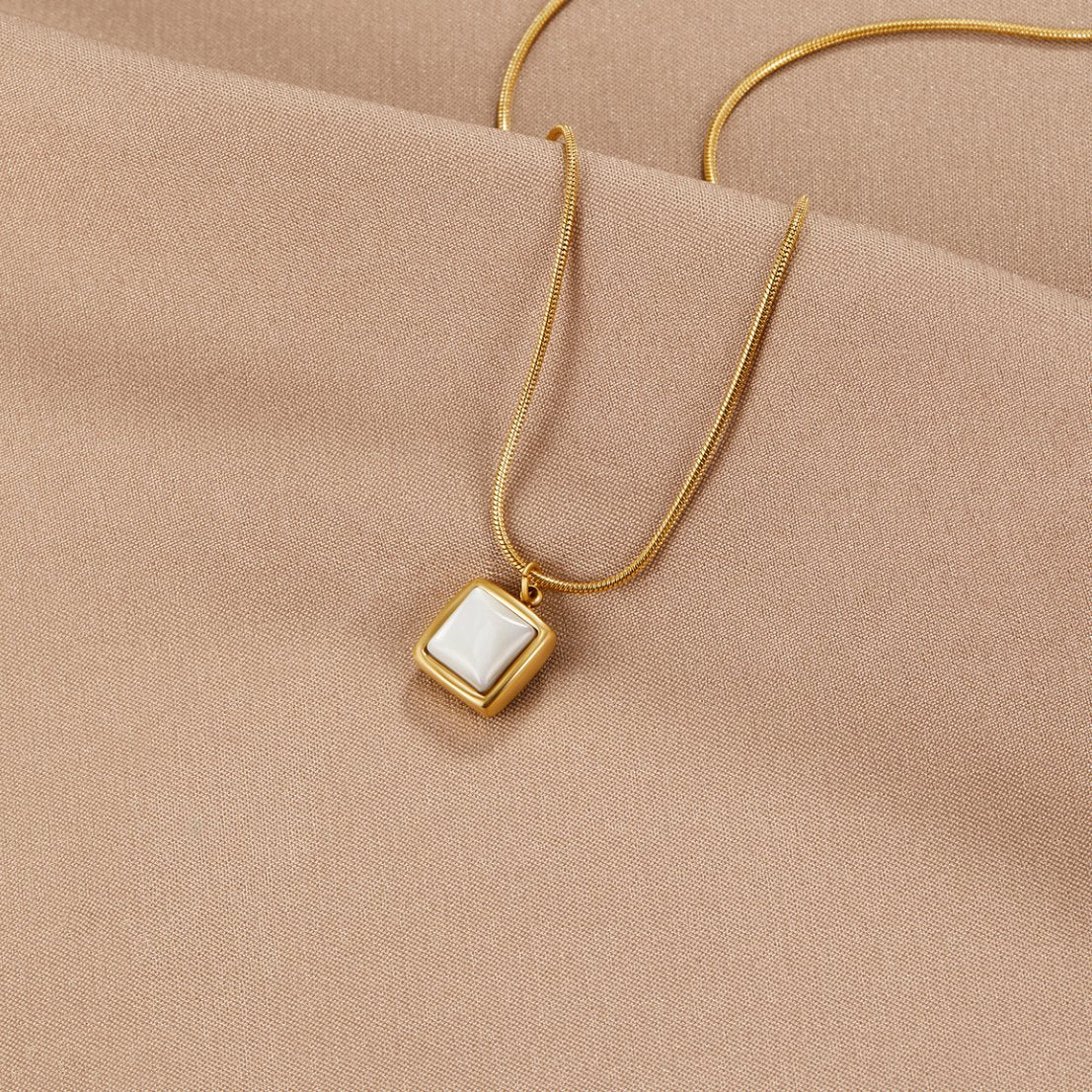 Riva Moonstone Pendant Necklace, laid on beige satin with a square white stone pendant