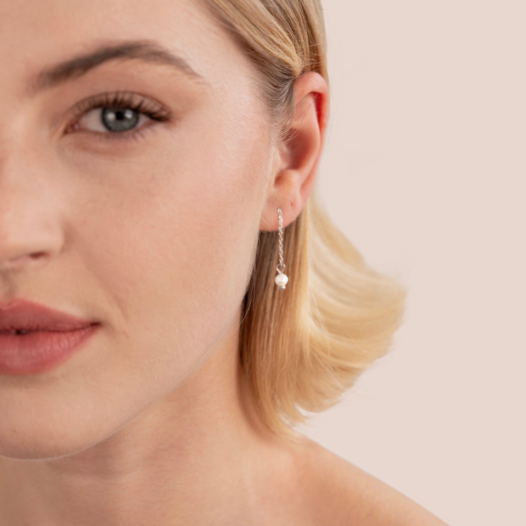 Silver Maria Pearl Drop Earrings, worn on a model's ear with a fine chain and small pearl drop