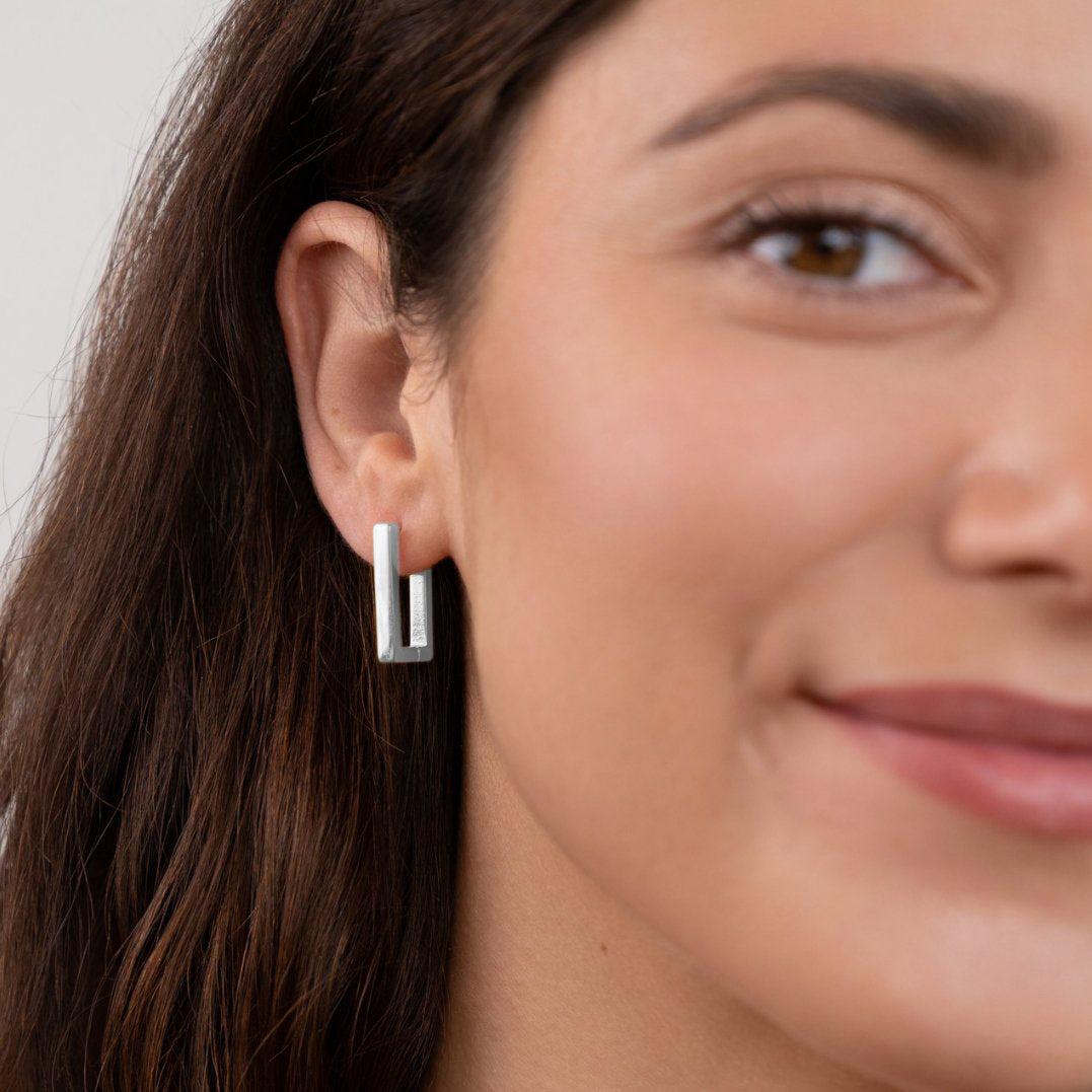 Silver Rectangle Hoop Earrings, worn on an ear by a smiling woman with long dark hair