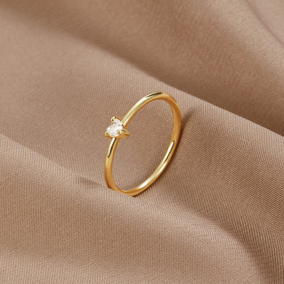 'Small Love' Crystal Heart Ring, thin gold band with small heart-cut stone on beige fabric