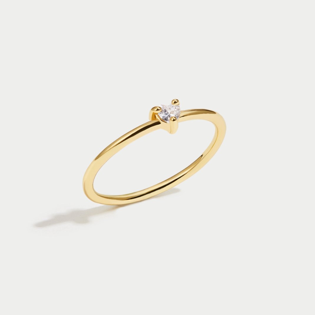 'Small Love' Crystal Heart Ring, thin gold band with a small clear heart stone, on plain background