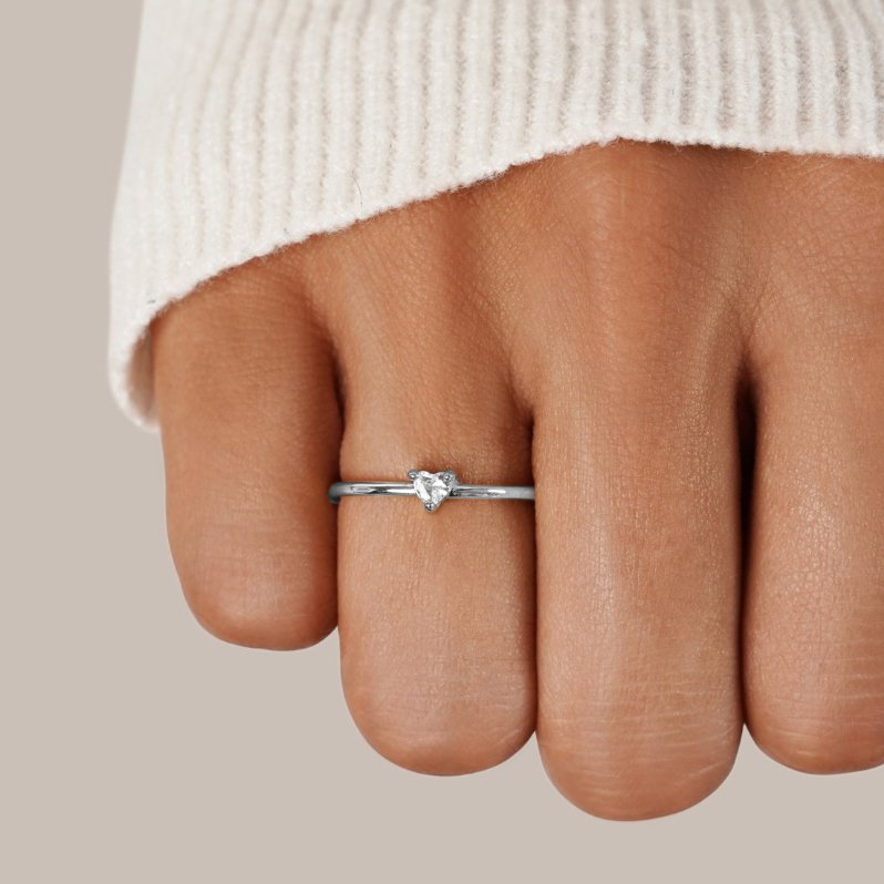 'Small Love' Crystal Heart Ring, worn on a hand in a cream knit sleeve, silver band