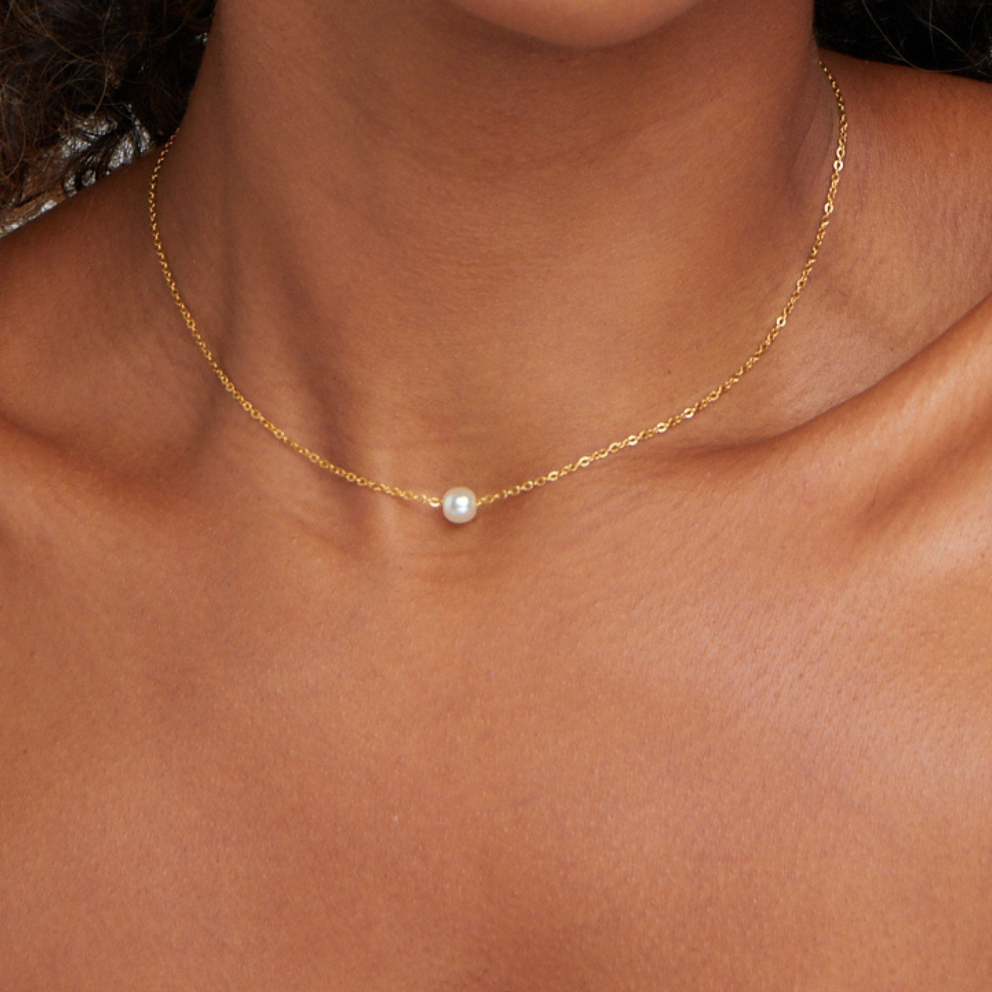Solitaire Gold Pearl Necklace, worn at the neck on a model, close-up with a single white pearl