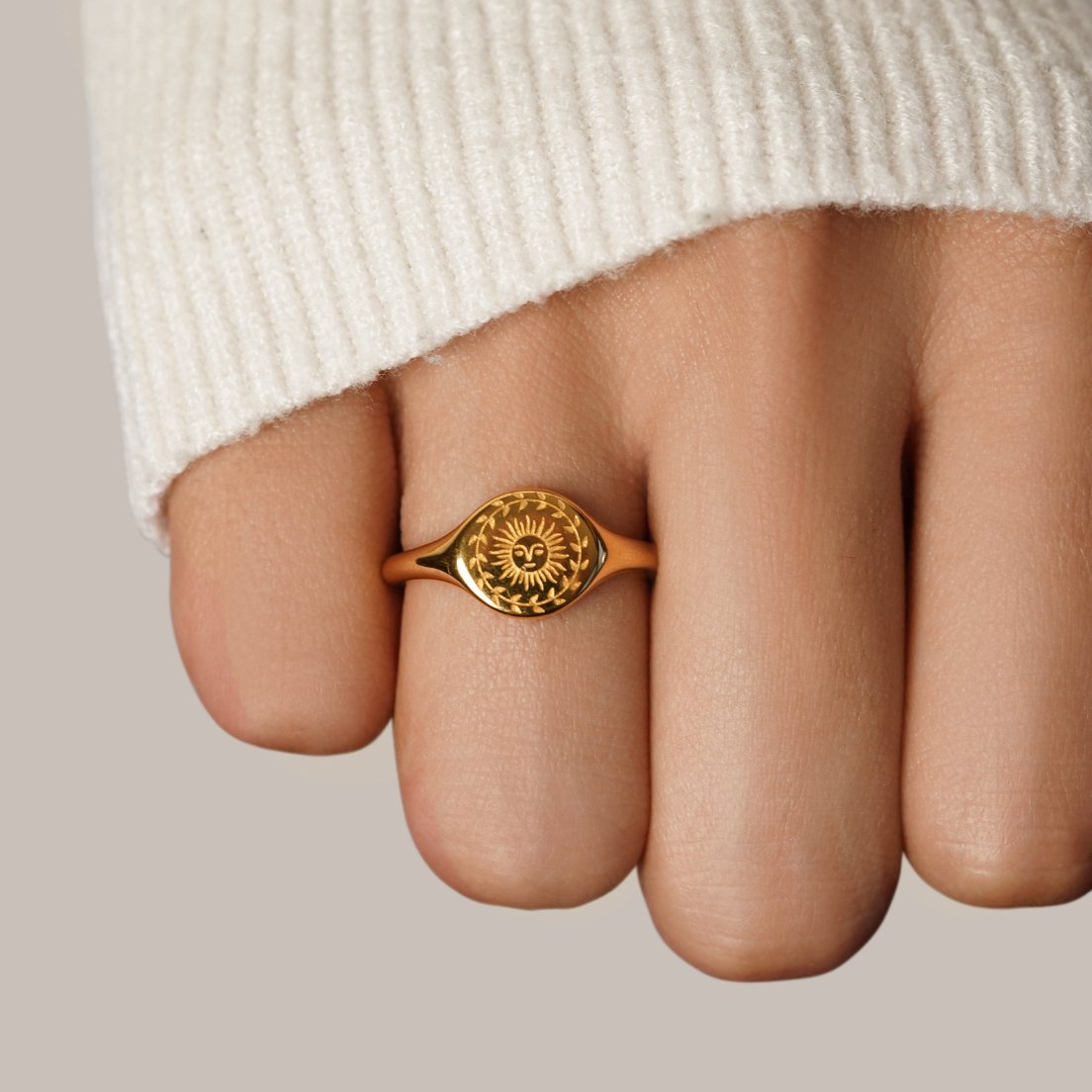 Summer Solstice Gold Ring, worn on a finger in a cream knit sleeve, engraved gold sun face