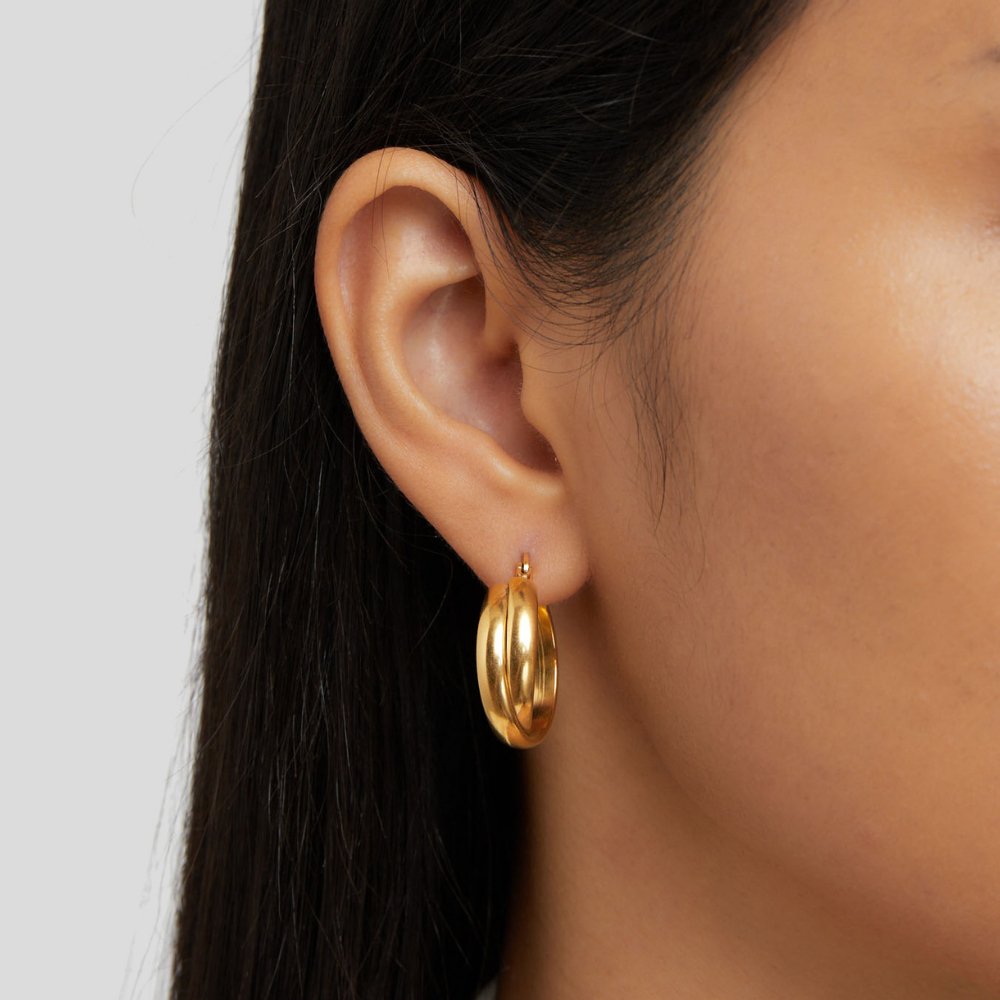 Talia Gold Hoop Earrings, worn on an ear, polished gold hoop with a thick rounded profile