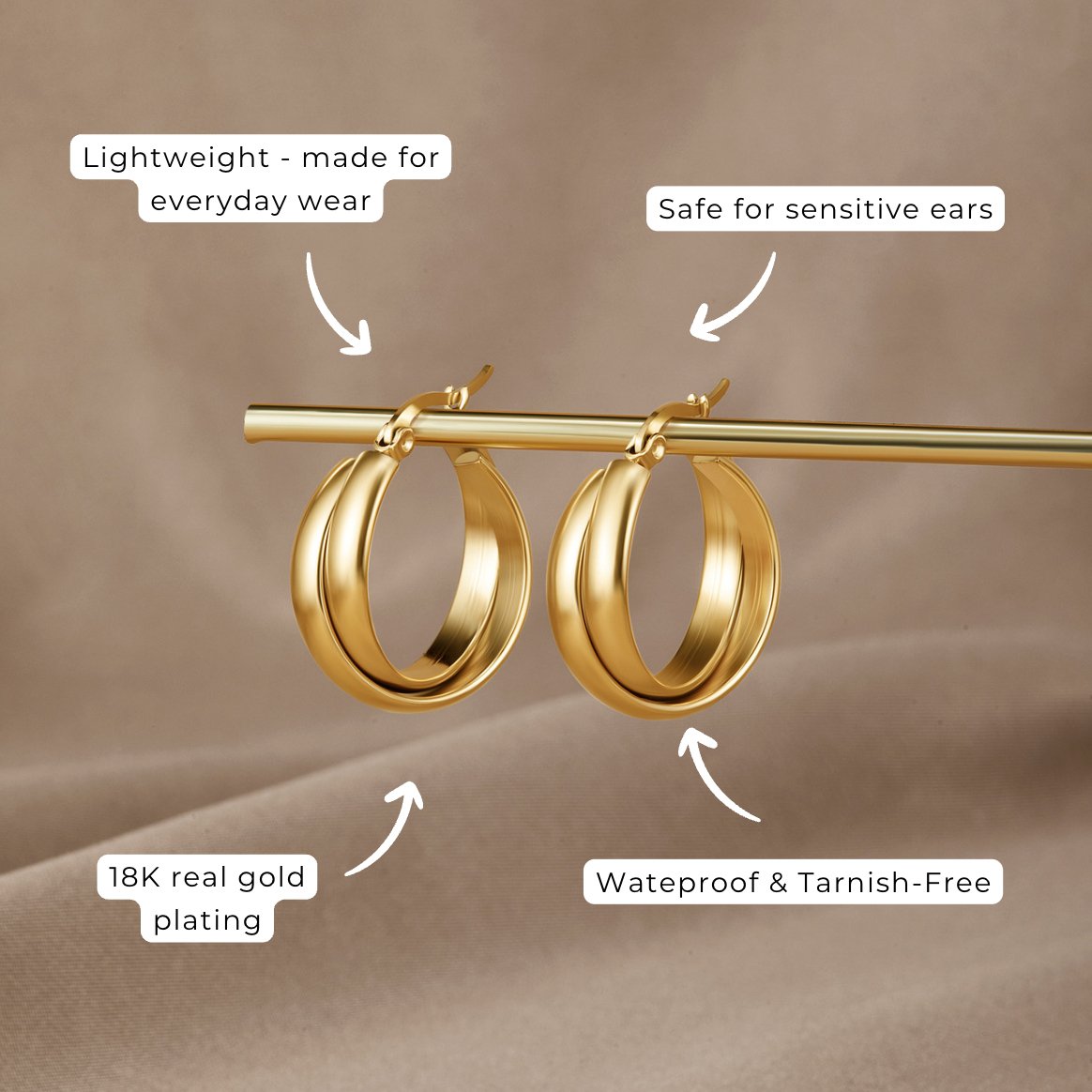 Talia Gold Hoop Earrings, a pair of gold hoops hanging from a gold rod, on a beige fabric backdrop