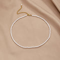 Temi Pearl Necklace, laid flat on beige satin, gold clasp and extender chain visible