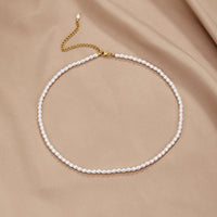 Temi Pearl Necklace, laid flat on beige satin, gold clasp and extender chain visible