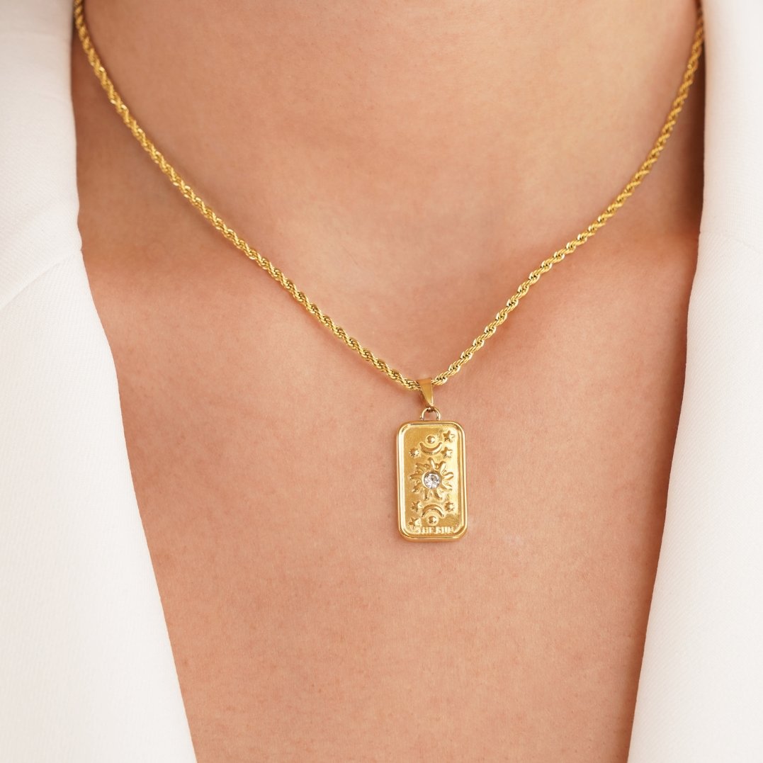 ‘The Sun’ Tarot Pendant Necklace, worn on a neck over a white jacket, close-up on the gold pendant
