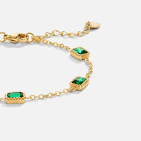 Trinity Emerald Bracelet, close-up of gold chain bracelet with green emerald-cut stones on white