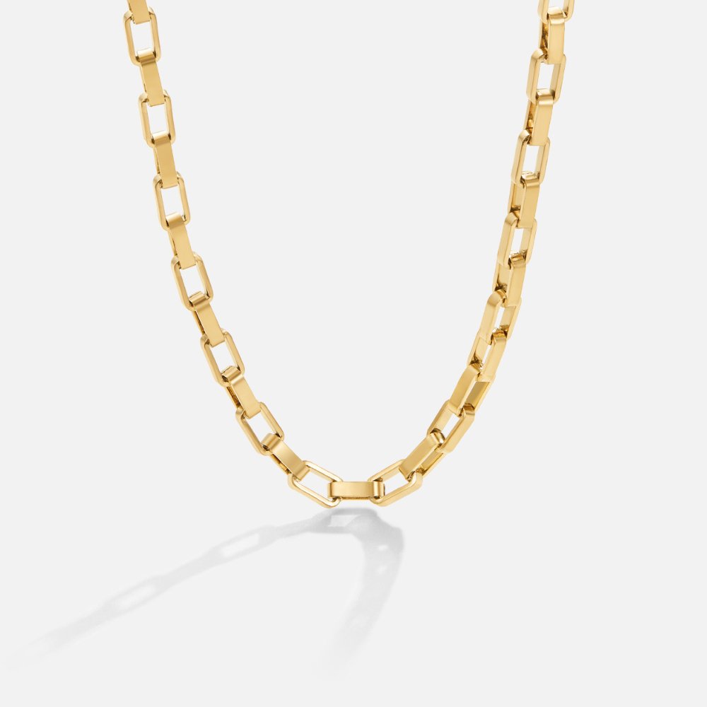 Venna Gold Chain Necklace, gold rectangular-link chain lying in a curve on white, with shadow