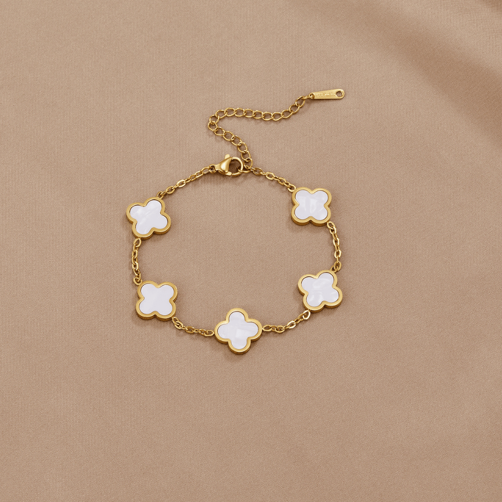 White Clover Bracelet, laid flat on beige fabric, five white clover charms on gold chain