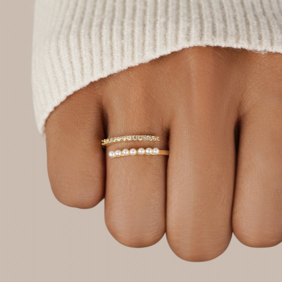 “Wrap Me” Pearl & Crystal Ring, worn on a finger in a cream knit sleeve, gold with pearls and stones